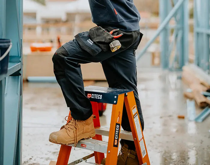 Man stood on a small ladder, wearing Hard Yakka workwear and work boots
