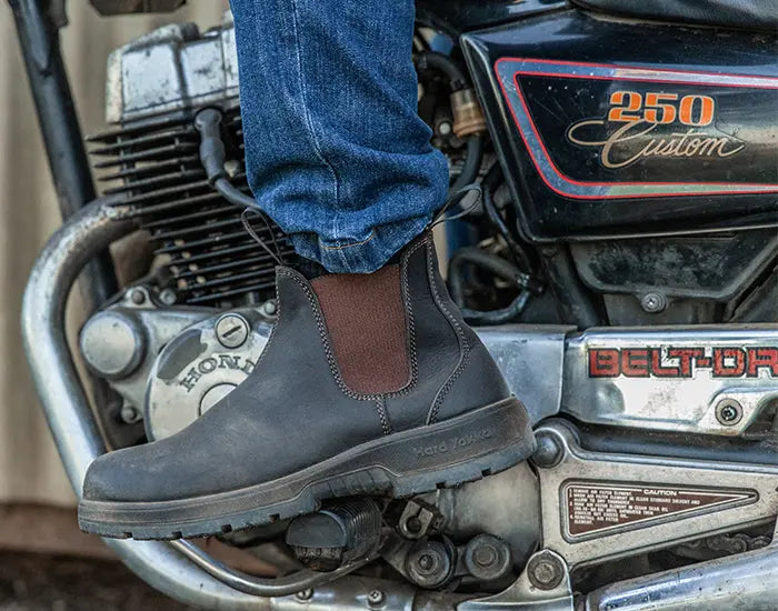 Close up image of a person wearing a Hard Yakka Dealer Boot resting on a calssic motorcycle foot rest